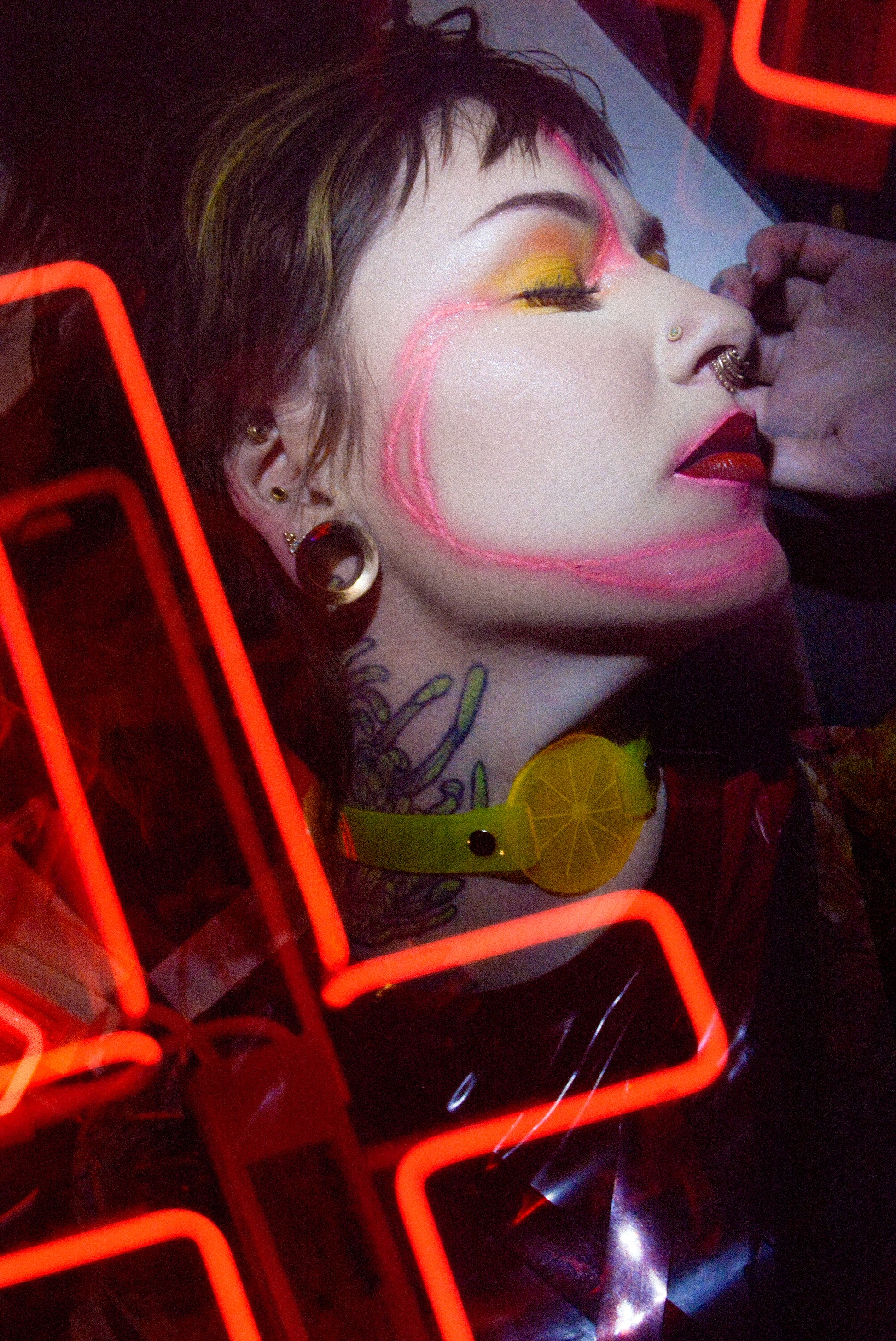Katrina models a neon uv yellow citrus choker by Apatico and Anhedonie, a floral dress by Samantha Rei, and a red neon cross light under blue and red neon lights at night.