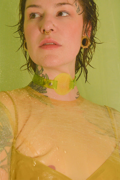 Katrina wears an Apatico and Anhedonie citrus collar choker in neon green, while wearing a yellow latex top and yellow dress.