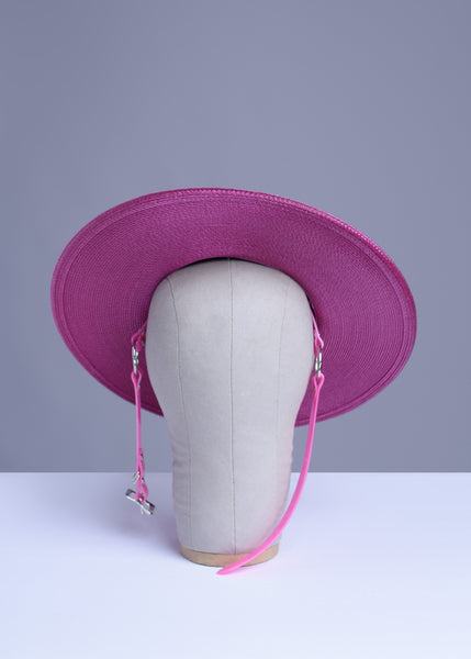 Fuchsia magenta pink harness hat with pink buckle band, displayed on a wig stand.