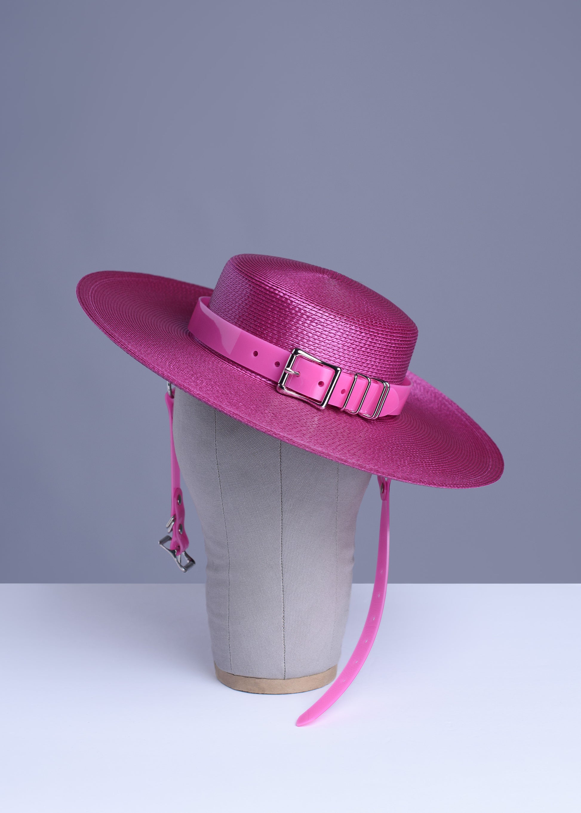 Fuchsia magenta pink harness hat with pink buckle band, displayed on a wig stand.