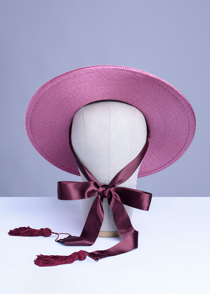 Apatico dusty mauve pink wide brim straw hat with burgundy satin ribbon ties and tassels.