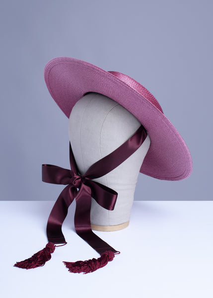 Apatico dusty mauve pink wide brim straw hat with burgundy satin ribbon ties and tassels.